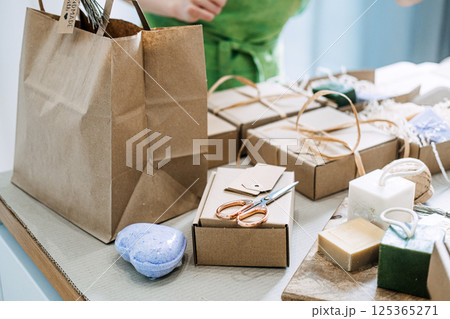 A collection of natural handmade soap bars, cardboard packaging, and eco-friendly gift wrapping tools on a tabletop. Sustainability, small business support, artisan craftsmanship, zero waste packaging 125365271