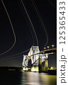 夜の東京ゲートブリッジを通過する飛行機の光跡 125365433