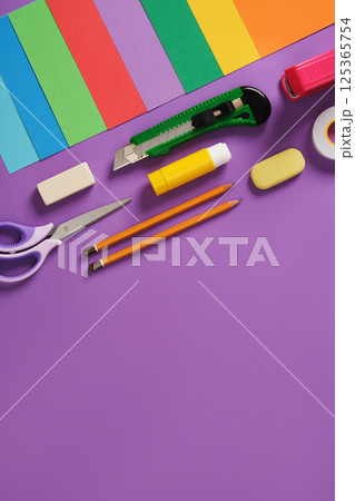 Paper craft table: scissors, knife, pencil, eraser, colored paper on purple background. Space for your text. 125365754