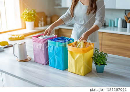 A woman is sorting trash into three different colored trash bags 125367961