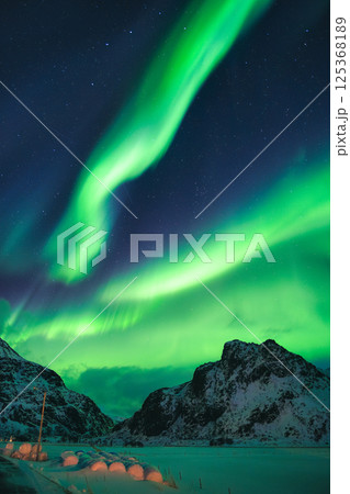 Northern Lights glowing over snowy mountain in winter at Lofoten Islands, Norway 125368189