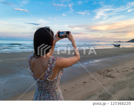 Asian woman taking a photo with mobile phone of tropical sea on the beach 125368220
