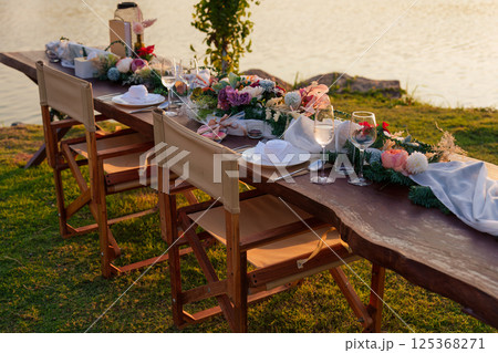 Romantic elegant dining setup with wooden long table, chairs, tableware, cutlery, candle and flora decoration Romantic elegant dining setup with wooden long table, chairs, tableware, cutlery, candle and flora decoration 125368271