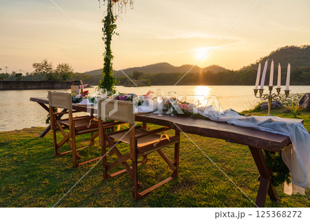 Romantic elegant dining setup with wooden long table, chairs, tableware, cutlery, candle and flora decoration 125368272