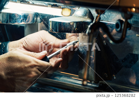 Technician using screwdriver removing nut from coffee maker in coffee shop 125368282