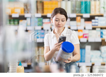 Woman checking baby formula ingredients with phone at pharmacy 125368472