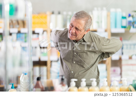 Senior man suffering from back pain while looking for medicine at drugstore Senior man suffering from back pain while looking for medicine at drugstore 125368512
