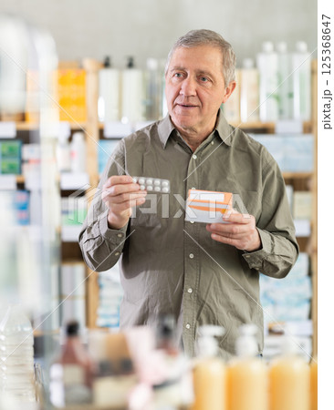Elderly man in a pharmacy chooses pills Elderly man in a pharmacy chooses pills 125368647