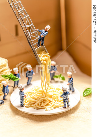 A group of small figurines are working together to pull noodles out of a plate 125368684