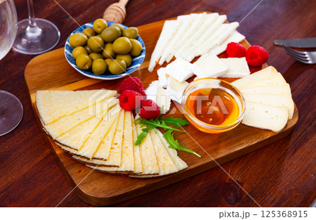 Various types of cheese, honey, raspberries and olives on wooden board Various types of cheese, honey, raspberries and olives on wooden board 125368915