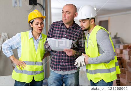 Man with papers talking to builders in house during renovation 125368962