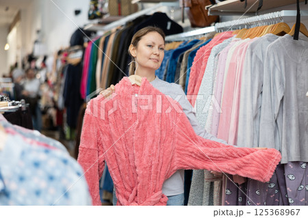 Middle-aged woman choosing convenient bathrobe in clothing store 125368967