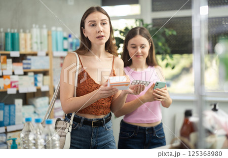 Daughter with her mother in summer dress choose pills in pharmacy 125368980