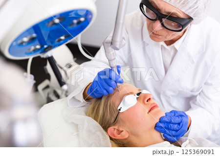 Cosmetologist doing laser wart removal procedure for young woman Cosmetologist doing laser wart removal procedure for young woman 125369091