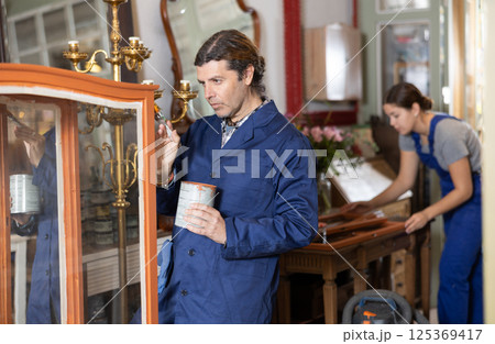 middle-aged furniture maker applies varnish with brush to wooden parts of vintage cabinet middle-aged furniture maker applies varnish with brush to wooden parts of vintage cabinet 125369417