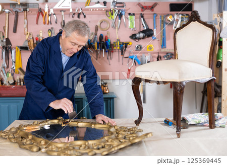restorer carefully covers carved wooden frame of antique wall mirror with layer of varnish restorer carefully covers carved wooden frame of antique wall mirror with layer of varnish 125369445