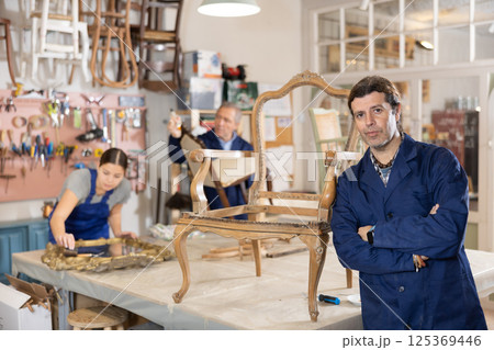 Portrait of middle-aged skillful repairman carpenter posing with crossed hands during workday in furniture woodwork studio Portrait of middle-aged skillful repairman carpenter posing with crossed hands during workday in furniture woodwork studio 125369446