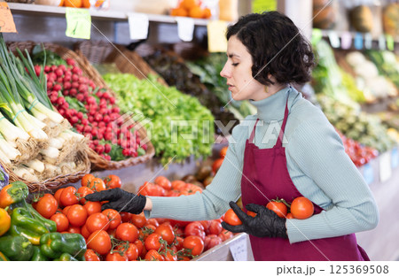 Woman shop seller puts tomato goods on display case 125369508