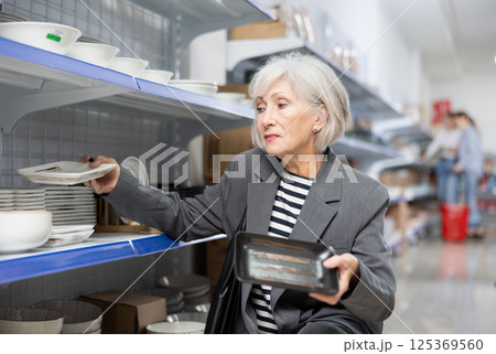Enthusiastic senior lady choosing square ceramic plates at Asian store Enthusiastic senior lady choosing square ceramic plates at Asian store 125369560