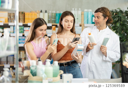 Woman with teen girl choosing and scan QR code cream at pharmacy. Man pharmacist offer European brand 125369589
