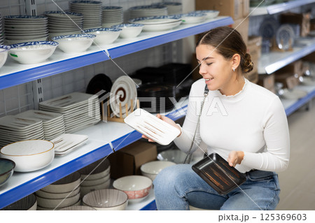 Young girl choosing square ceramic Asian style plates in store Young girl choosing square ceramic Asian style plates in store 125369603
