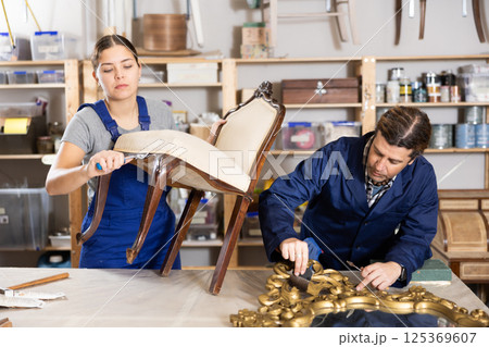 Professional male and female artisans restorers in uniform renovating antique chair mirror frame while working in repair shop 125369607