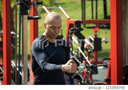 Adult caucasian man training exercising crossover trainer at public gym park. Outdoors activity. Fitness coach make exercise. Adult caucasian man training exercising crossover trainer at public gym park. Outdoors activity. Fitness coach make exercise. 125369740