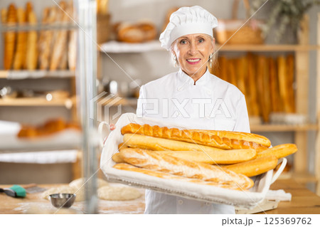Senior female baker worker shows baguette Senior female baker worker shows baguette 125369762