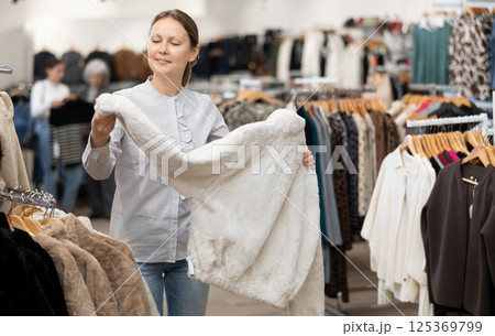 Middle-aged woman choosing short fur coat in clothing shop 125369799