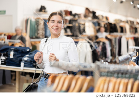Positive joyful young woman looking for fashionable clothes in clothing boutique Positive joyful young woman looking for fashionable clothes in clothing boutique 125369822