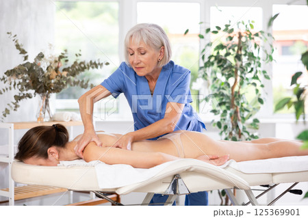 Unrecognizable young woman lies face down and enjoy shoulder massage for body care Unrecognizable young woman lies face down and enjoy shoulder massage for body care 125369901