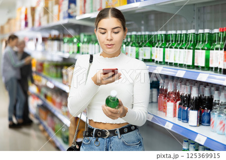 Girl customer take photo of unusual Korean soy wine chum churum and examine product. Girl customer take photo of unusual Korean soy wine chum churum and examine product. 125369915