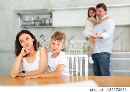 Son soothe his mother after a domestic quarrel. Father with little daughter in background 125370081