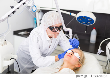 Cosmetologist making laser mole removal procedure for young woman 125370088