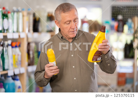 Elderly man buys a cleaning product for washing parquet and laminate floors in supermarket Elderly man buys a cleaning product for washing parquet and laminate floors in supermarket 125370115
