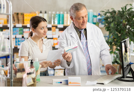 Male pharmacist helps female customer find prescription medication 125370118