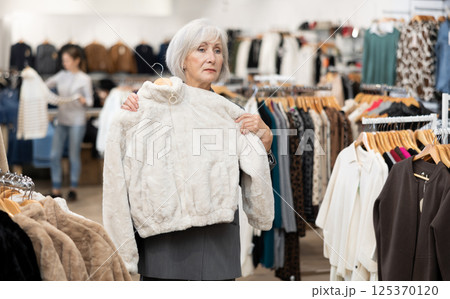 Elderly woman choosing fur coat in store 125370120