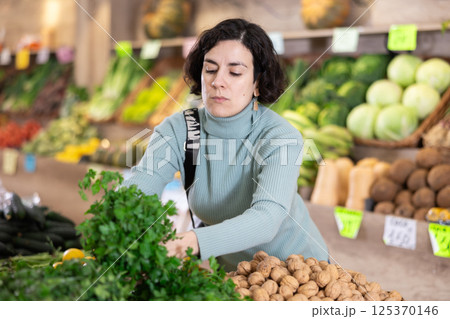 Adult woman chooses parsley in vegetable shop Adult woman chooses parsley in vegetable shop 125370146
