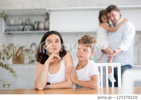 Son soothe his mother after a domestic quarrel. Father with little daughter in background Son soothe his mother after a domestic quarrel. Father with little daughter in background 125370220