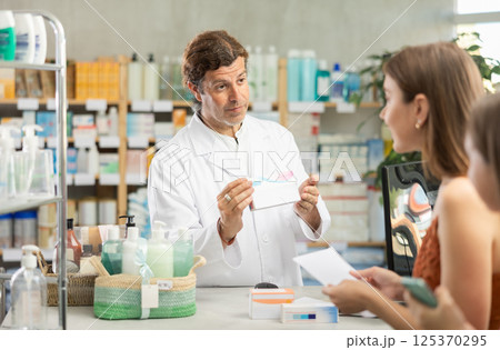 In drug store, man at counter sells medication, offer remedy to customer In drug store, man at counter sells medication, offer remedy to customer 125370295