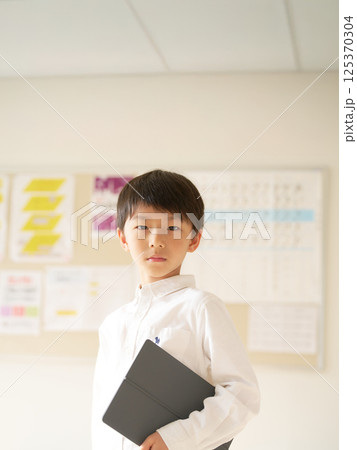 タブレット端末を抱えて視線を向ける男子小学生 125370304