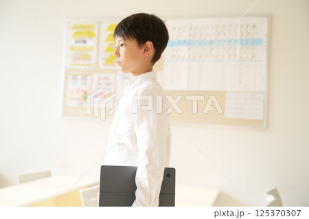 タブレット端末を抱えて前を見る男子小学生 125370307