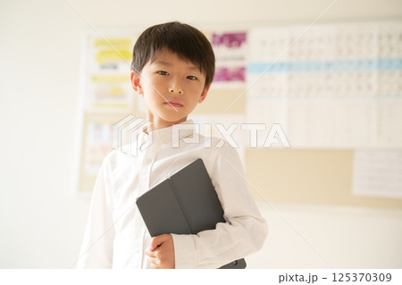 タブレット端末を抱えて視線を向ける男子小学生 125370309