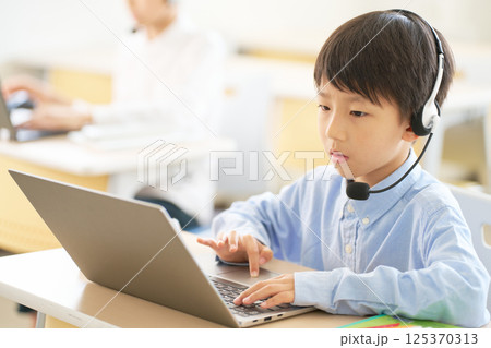 ヘッドセットをつけてPCを操作する小学生の男の子 ヘッドセットをつけてPCを操作する小学生の男の子 125370313