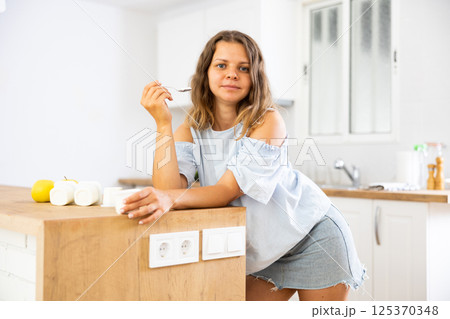 Young woman eating tasty yogurt in kitchen 125370348
