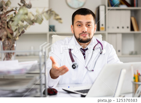 Cheerful man physician sitting at desk and explaining with gesture 125370383