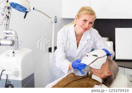 Cosmetologist putting spectrum mask on senior woman's face 125370410