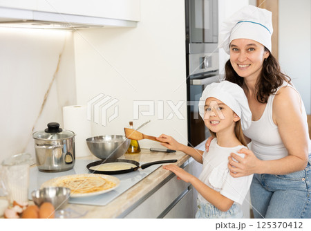 Happy mother and daughter frying pancakes in the kitchen Happy mother and daughter frying pancakes in the kitchen 125370412