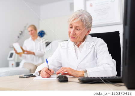 Senior woman dermatologist writing notes during appointment 125370418