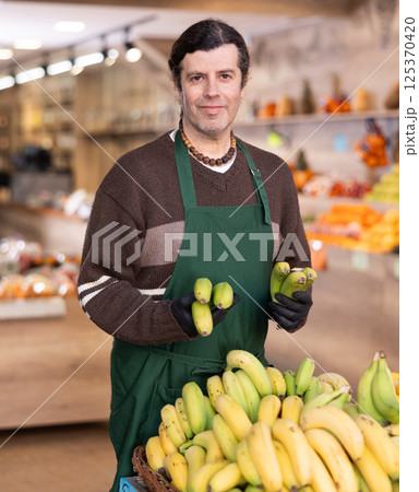 Man shop seller puts banana goods on display case 125370420